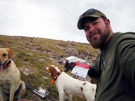 Hunter with two hunting dogs and a harvested white-tailed ptarmigan